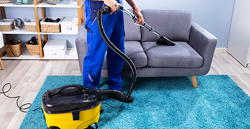 woman vacuuming living room while man is lying couch
